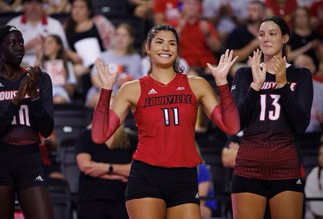 Louisville volleyball players smiling and clapping on court.