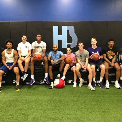 Group of people seated in gym with basketballs.