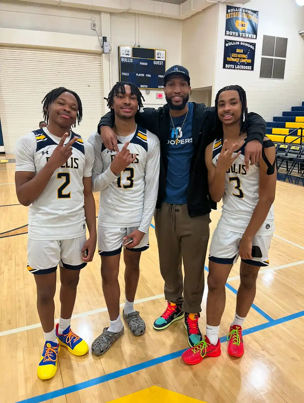 Basketball players pose on court with coach.