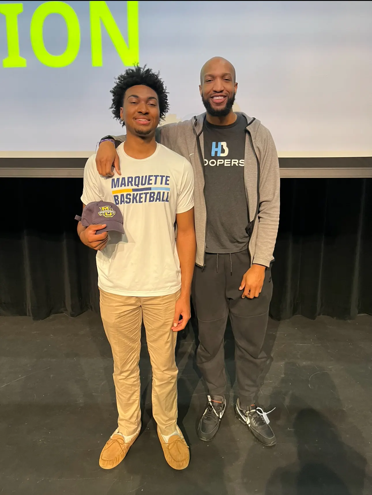 Two men on stage, one wearing Marquette Basketball shirt.