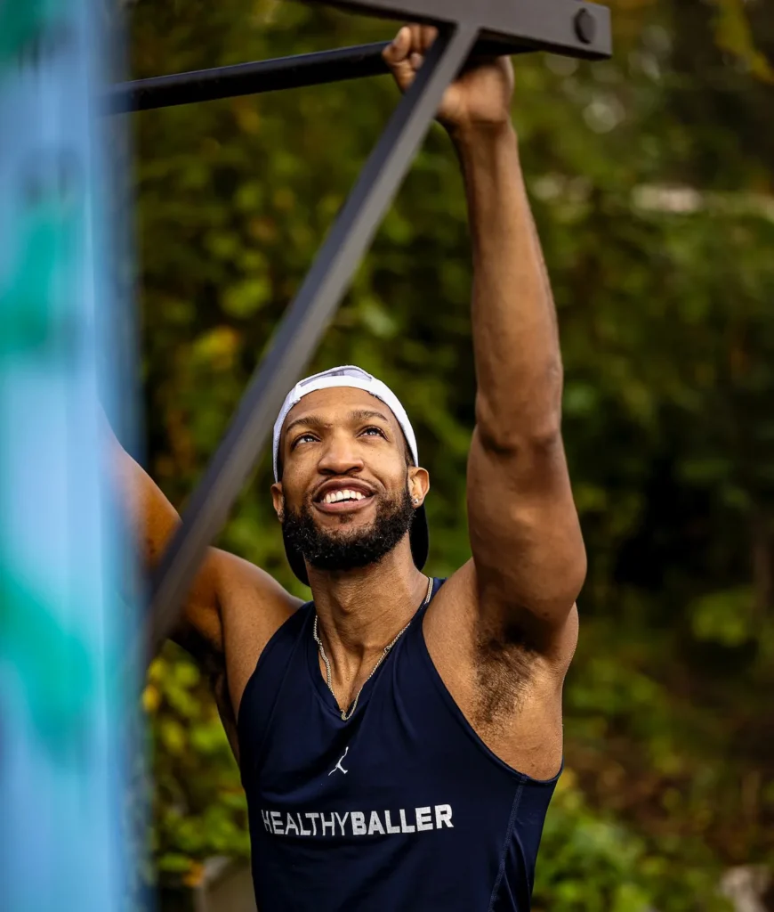 Man doing pull-ups outdoors, wearing athletic tank top.
