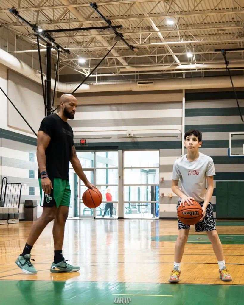 Basketball coach training young player in gym.