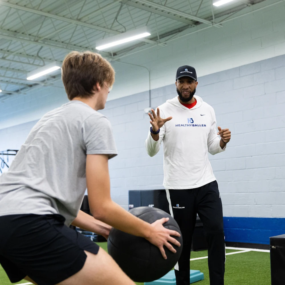Coach instructing athlete with medicine ball indoors.