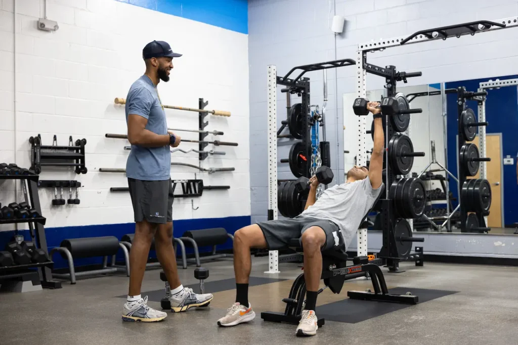 Trainer guides workout in gym with dumbbells.