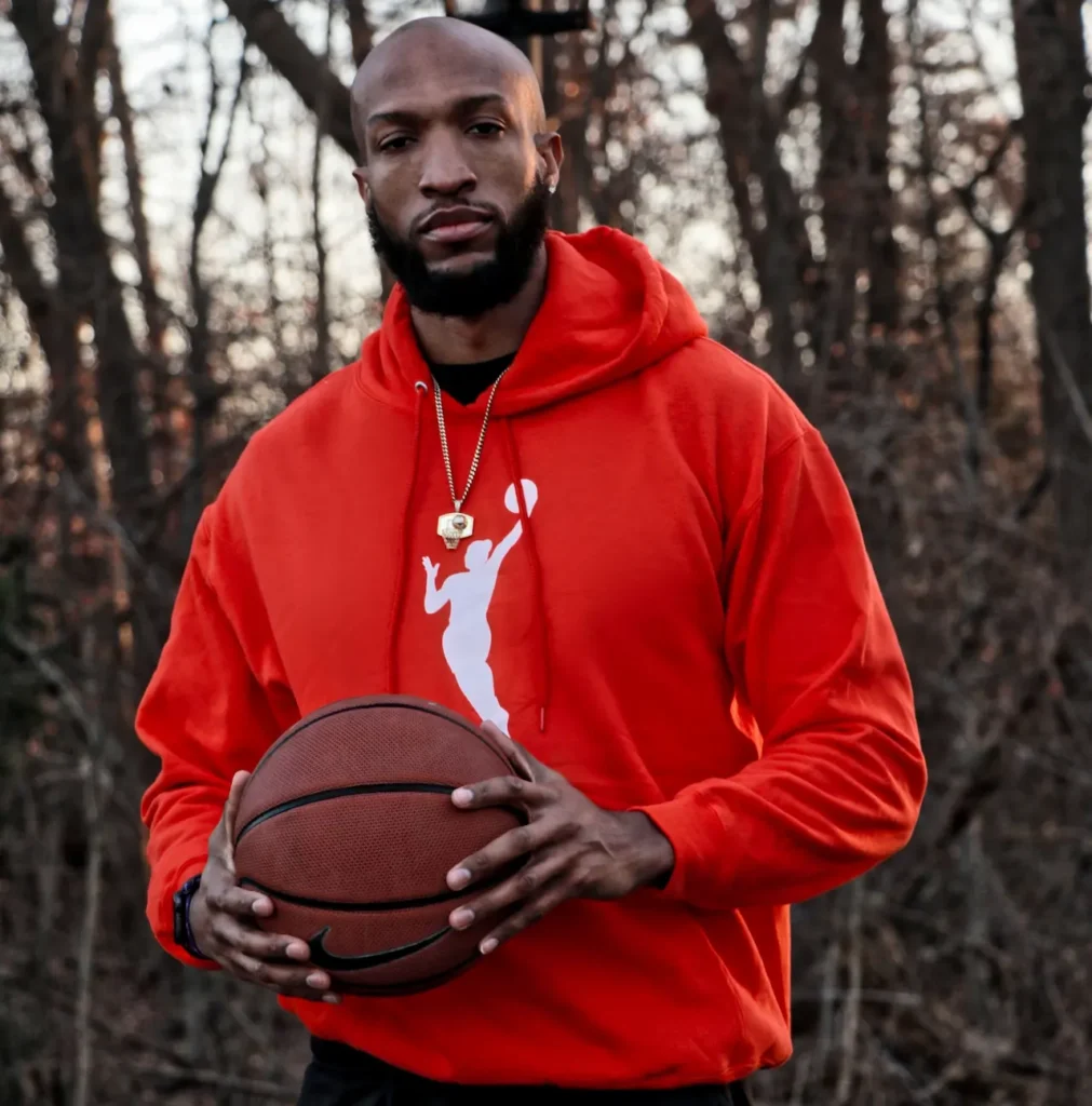 Man in red hoodie holding basketball outdoors.