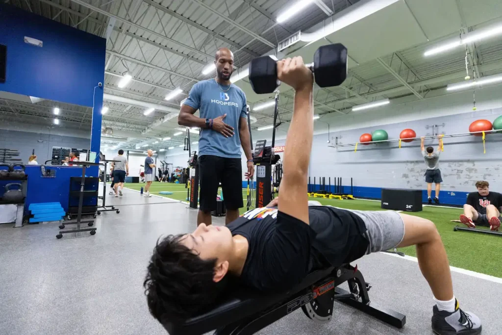 Trainer supervising gym workout with dumbbells.