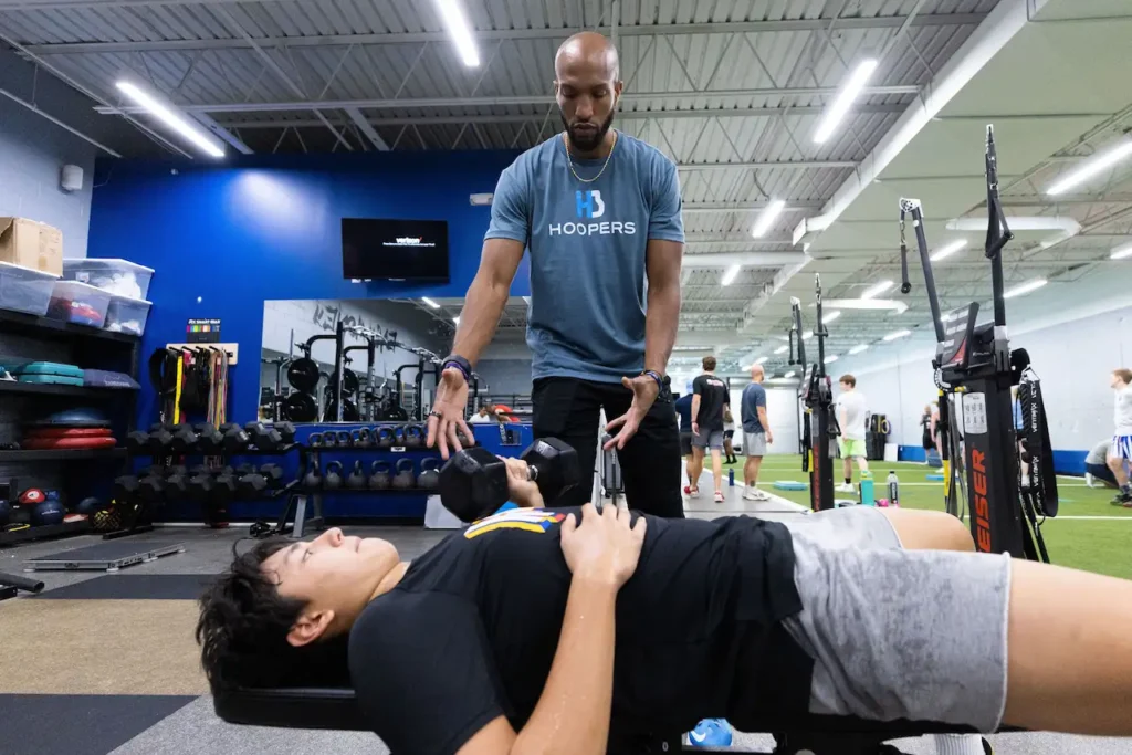 Trainer assists with dumbbell workout in gym.