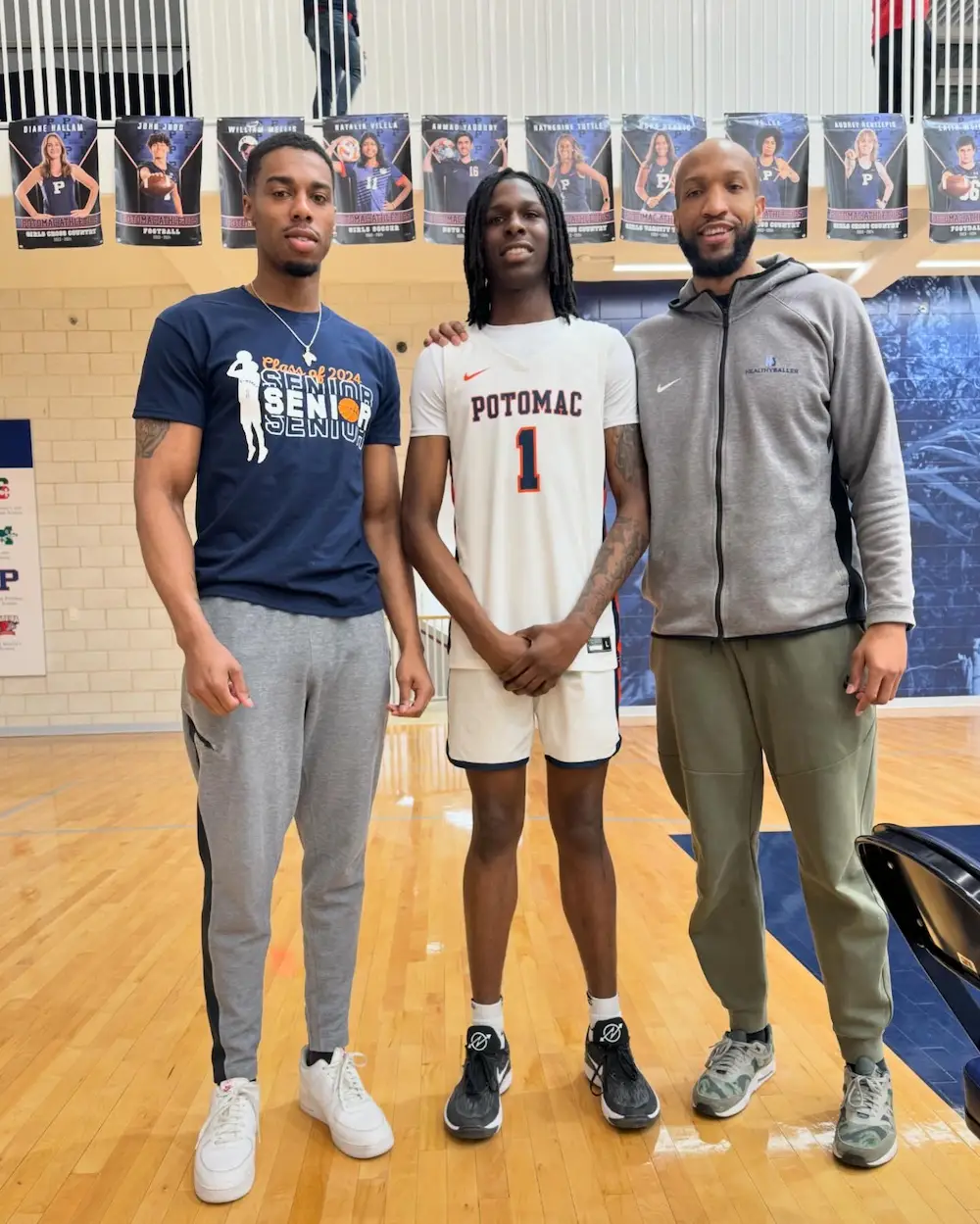 Basketball player posing with two men in gym.