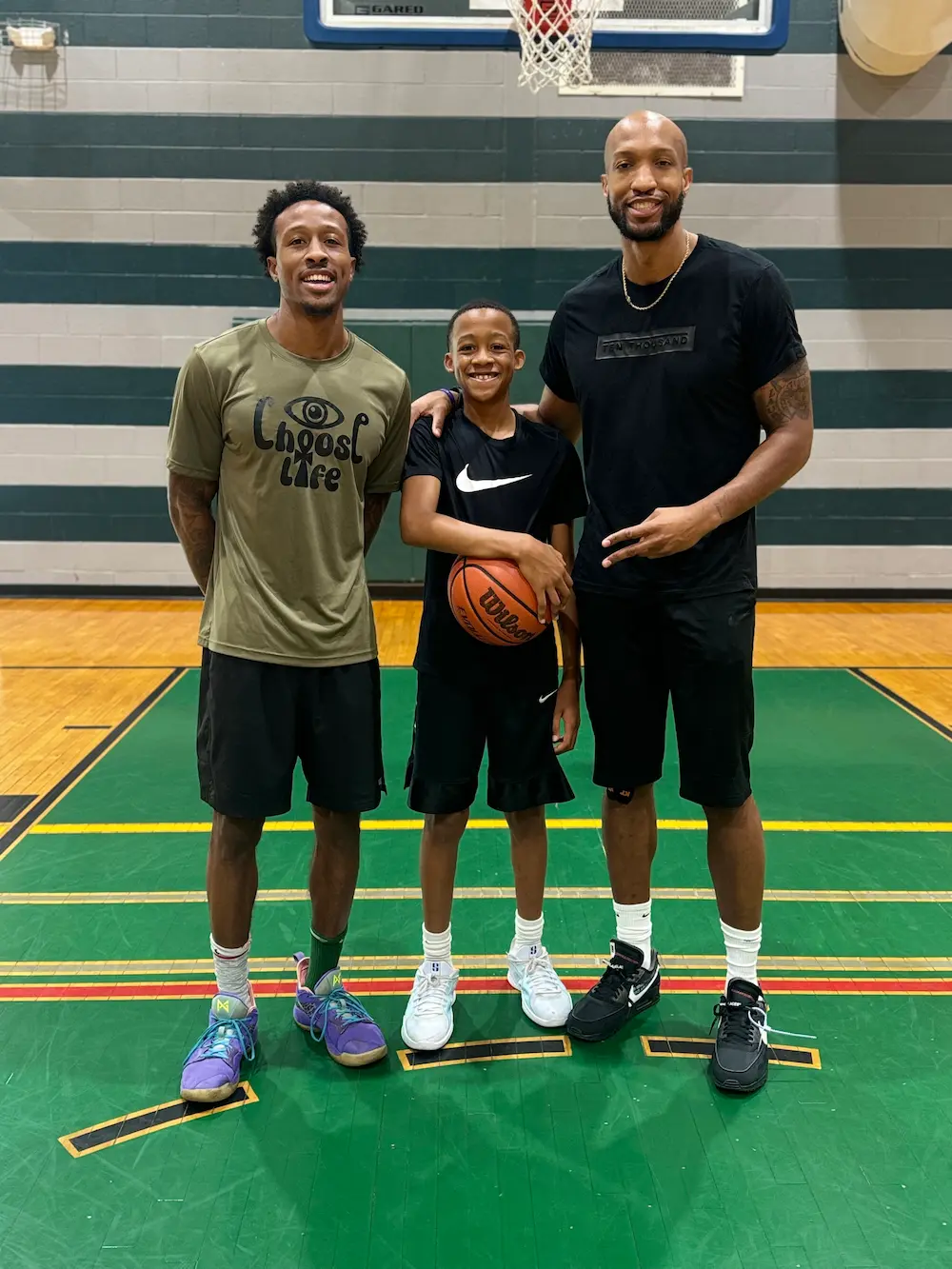 Three people posing with a basketball in gym.
