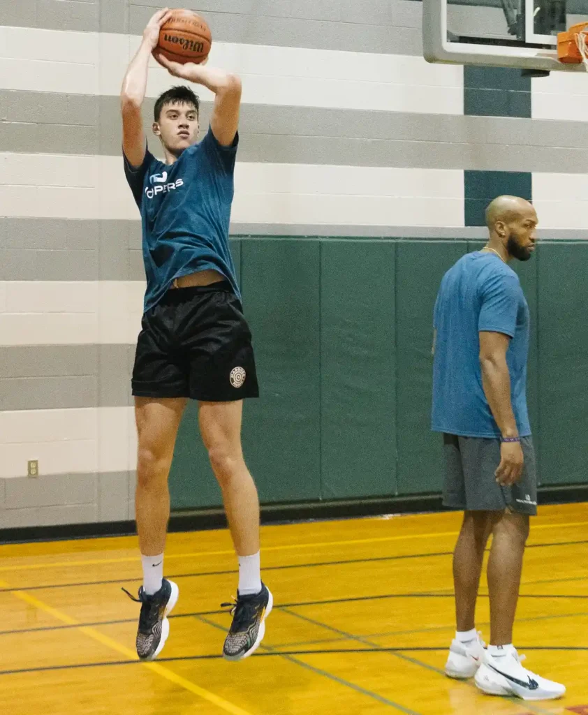 Basketball player practicing jump shot in gym.